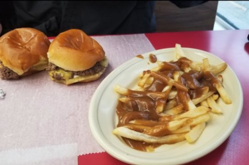 Two cheeseburger sliders on a table next to a plate of fries topped with gravy.