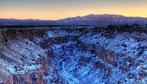 A snowy canyon landscape at sunset, with mountains in the background and a river winding through the valley.