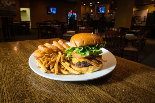 A juicy burger with lettuce and tomato, served with crispy fries on a wooden table in a restaurant setting.