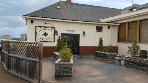 Exterior of a restaurant with a welcoming sign, surrounded by planters and a fence, under a cloudy sky.