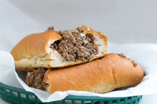 Two loaded sandwich rolls filled with shredded beef, resting in a green basket lined with white paper.