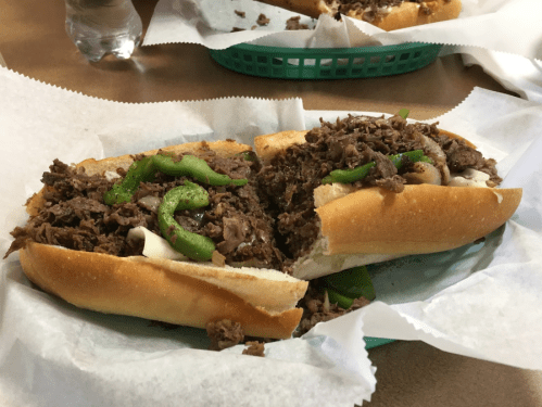 Two loaded sandwiches with beef, green peppers, and mayonnaise, served in a green basket lined with white paper.