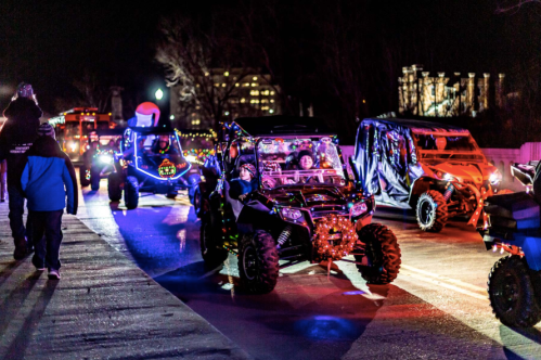 A festive night parade featuring decorated off-road vehicles with colorful lights and holiday decorations.