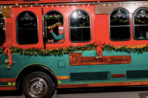 A festive trolley decorated with lights and garlands, with a smiling driver wearing a Santa hat.