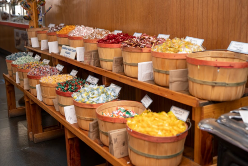 A colorful display of various candies in wooden baskets on shelves at a candy store.