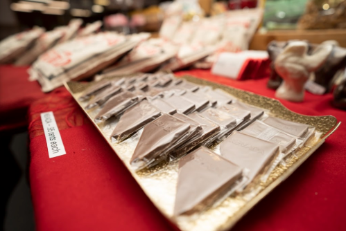 A tray of neatly arranged chocolate pieces on a red tablecloth, with decorative items in the background.