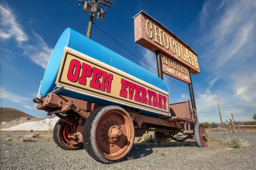 A vintage truck with a blue tank parked under a "Chocolate Nugget Candy Factory" sign that says "Open Everyday."