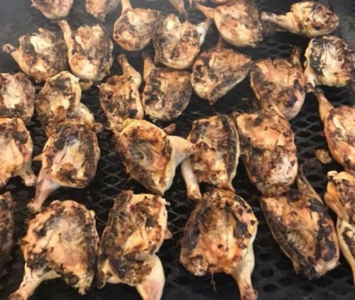 Grilled chicken pieces with a charred, smoky appearance on a barbecue grill.
