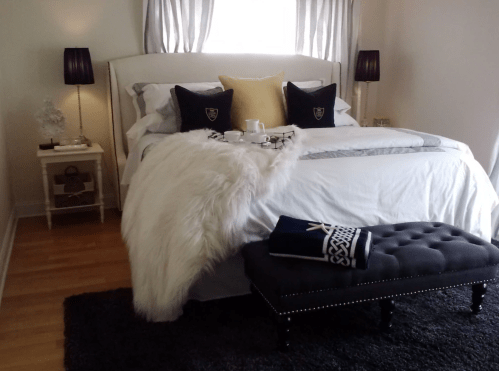 Cozy bedroom with a plush bed, decorative pillows, a fur throw, and a stylish bench at the foot of the bed.
