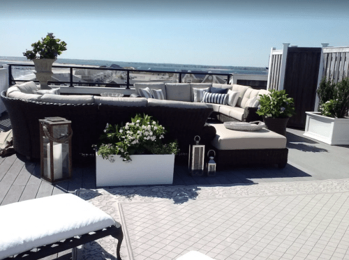 A stylish rooftop patio with a curved sofa, potted plants, and a scenic view of the horizon.