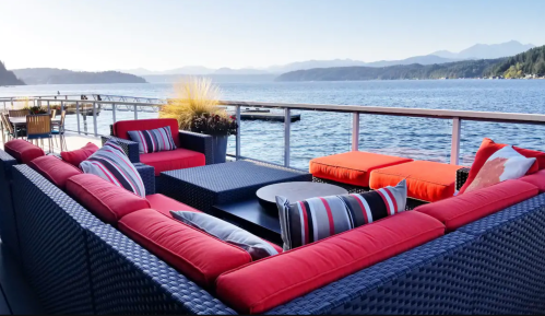A cozy outdoor seating area with red cushions overlooks a serene lake and mountains in the background.