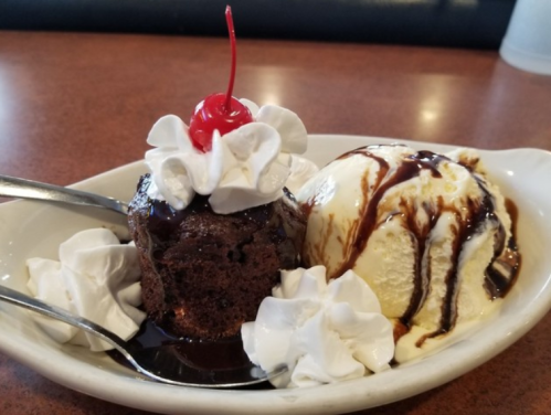 A dessert featuring a chocolate cake topped with whipped cream and a cherry, served with a scoop of vanilla ice cream and chocolate sauce.