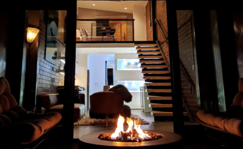 Cozy interior with a fire pit, modern staircase, and a view of a stylish living area above. Warm ambiance.