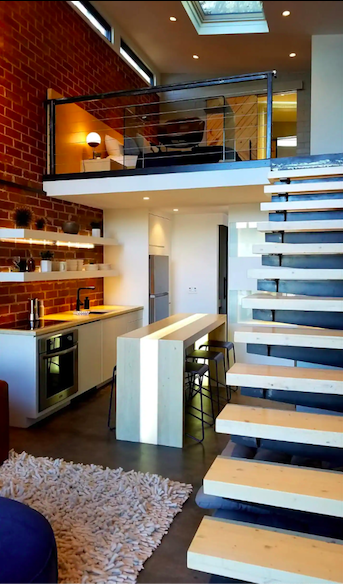Modern interior of a loft-style kitchen and living area with wooden stairs, brick walls, and sleek furnishings.