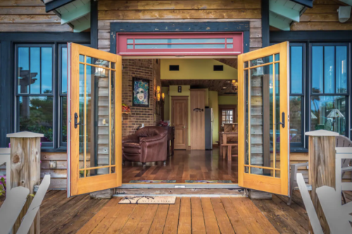 Open double doors reveal a cozy interior with wooden floors and a leather couch, framed by a rustic exterior.