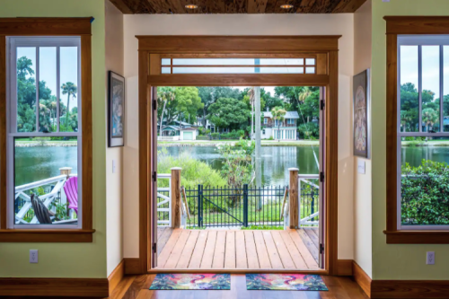 View from a home entrance overlooking a serene lake, framed by large windows and wooden doors.