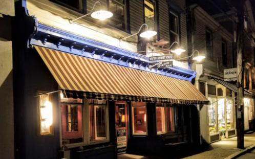 A charming restaurant with a blue facade and striped awning, illuminated at night in a quaint street setting.