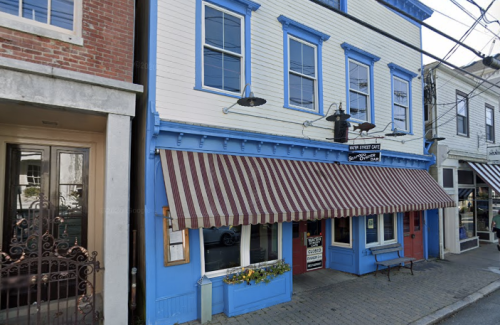 A colorful café with blue and white exterior, striped awning, and flower boxes, located on a charming street.