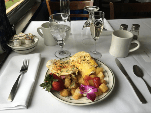 A plate with eggs, fruit, and toast, set on a table with water, coffee, and condiments in a restaurant setting.