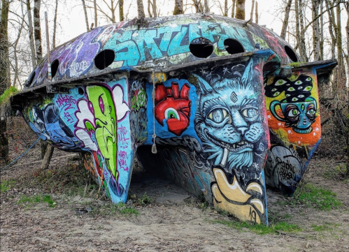 A colorful, graffiti-covered structure resembling a UFO, surrounded by trees and nature.