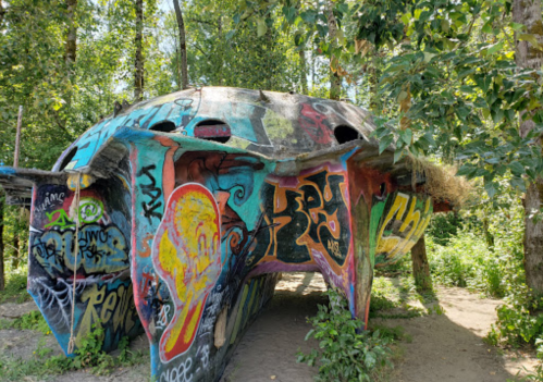 A colorful, graffiti-covered structure surrounded by trees and greenery, resembling a whimsical, abstract shape.