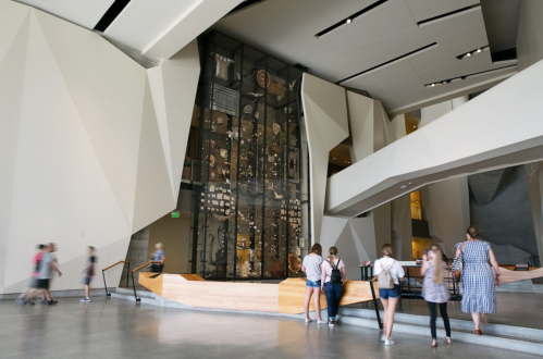 Visitors explore a modern museum interior featuring geometric architecture and a large display of artifacts.