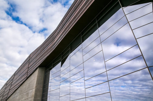 Modern building with a curved roof, featuring large reflective windows and a cloudy sky in the background.