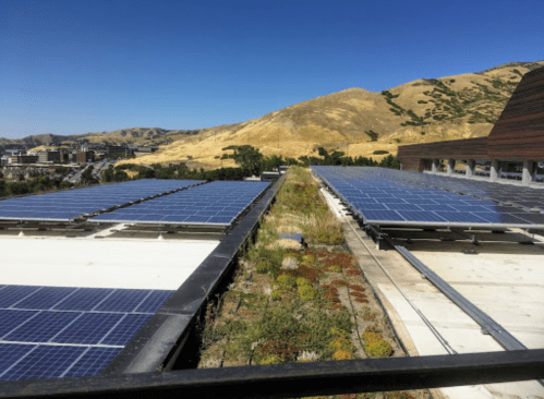 A rooftop with solar panels and greenery, overlooking a hilly landscape under a clear blue sky.