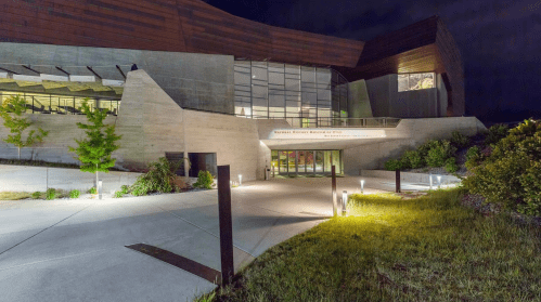Exterior view of the National Native American Museum at night, featuring modern architecture and illuminated pathways.
