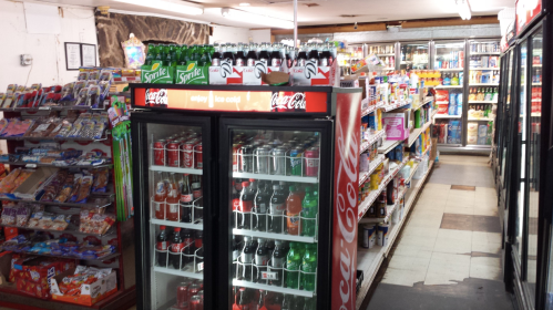 A convenience store aisle with shelves of snacks and drinks, featuring a Coca-Cola display fridge.
