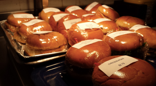 A tray of wrapped burgers with labels, showcasing various types and prices, in a warm, inviting setting.