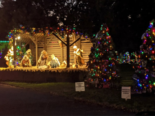 A festive nativity scene with colorful lights and decorated trees, set in a wooden structure.