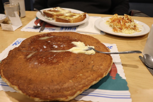 A large pancake with butter on top, served with toast and hash browns on a table.