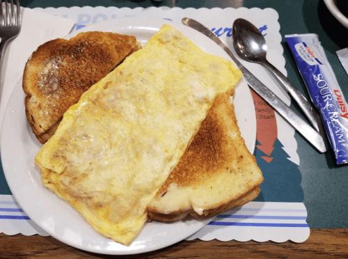 A plate with a fluffy omelet and two slices of toasted bread, accompanied by a packet of sour cream.