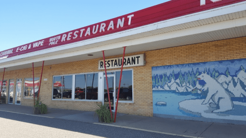 A restaurant with a large sign, featuring a polar bear mural on the wall and potted plants in front.