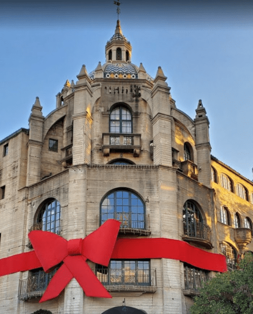 A historic building adorned with a large red bow, showcasing its architectural details against a clear sky.