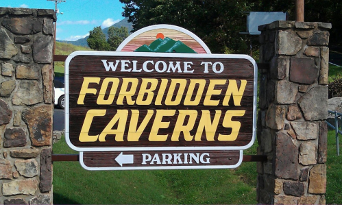 Sign welcoming visitors to Forbidden Caverns, featuring mountains and a parking direction.