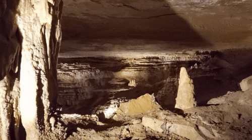A dimly lit cave interior with rock formations and stalactites, showcasing natural textures and shadows.