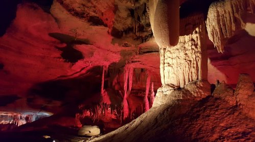 A dimly lit cave with red lighting, featuring stalactites and stalagmites, creating a dramatic underground landscape.