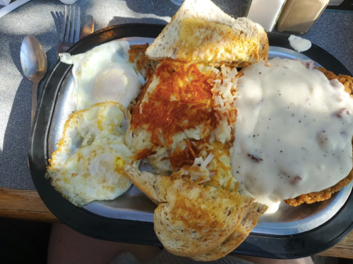 A breakfast plate featuring eggs, hash browns, toast, and chicken fried steak with gravy.