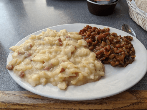 A plate with creamy potato dish and a side of baked beans, served on a gray table.