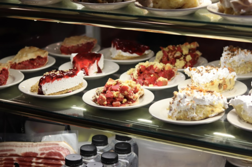 A display case filled with various desserts, including pies and cakes topped with fruit and whipped cream.