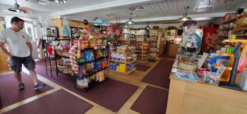 A cozy store interior with shelves of snacks and goods, and a customer browsing near the entrance.
