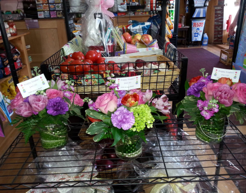A display of colorful flower arrangements in jars, with fresh produce in the background at a local shop.
