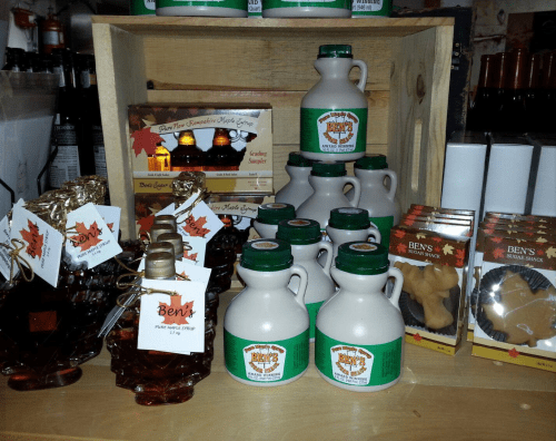 A display of maple syrup bottles and candy, featuring "Ben's" branding, arranged on a wooden crate.