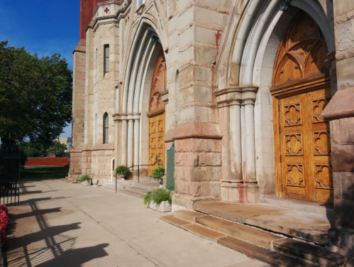 Exterior view of a stone church with wooden doors and a clear blue sky in the background.