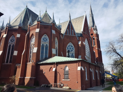 A large red brick church with pointed arches and stained glass windows, set against a blue sky.