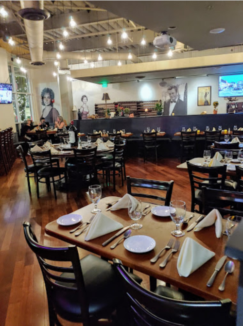 A spacious restaurant with wooden floors, neatly set tables, and vintage decor featuring black-and-white portraits on the walls.