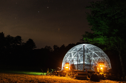 A geodesic dome illuminated by lanterns, set in a dark outdoor space with trees and a starry sky in the background.