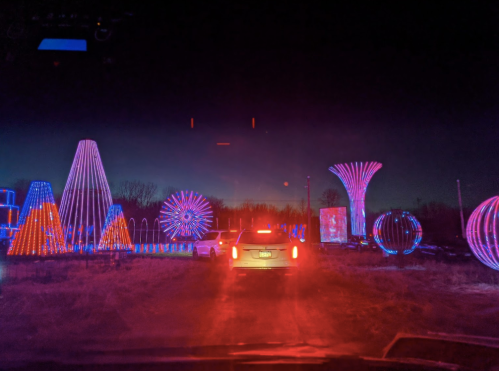 A car drives through a colorful light display at night, featuring various illuminated shapes and patterns.